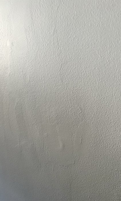Vit texturerad vägg med små fläckar och ojämnheter, enkel och monokrom.