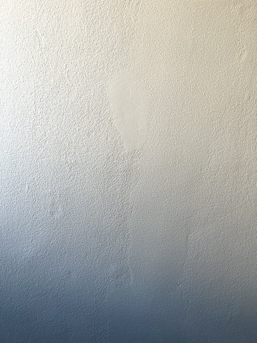 En ommålad fläck på en strukturerad vägg i nyanser av blått och vitt.