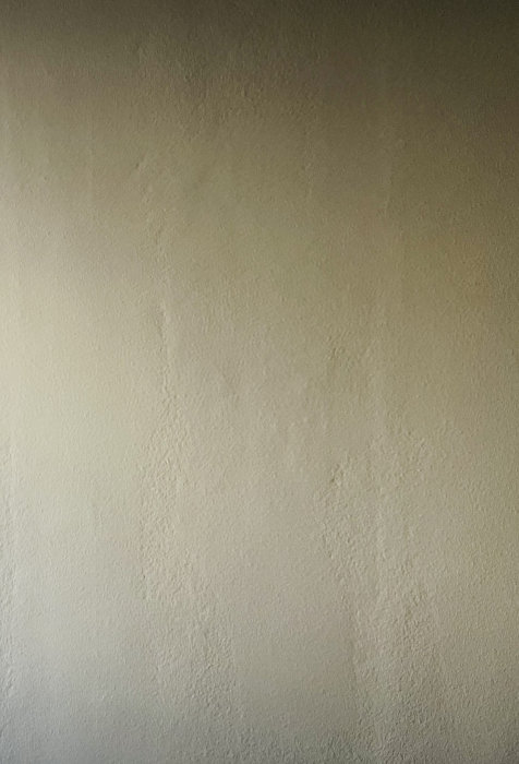 Enkel, ljus texturerad vägg, skuggor, måttlig belysning, inga distinkta objekt.
