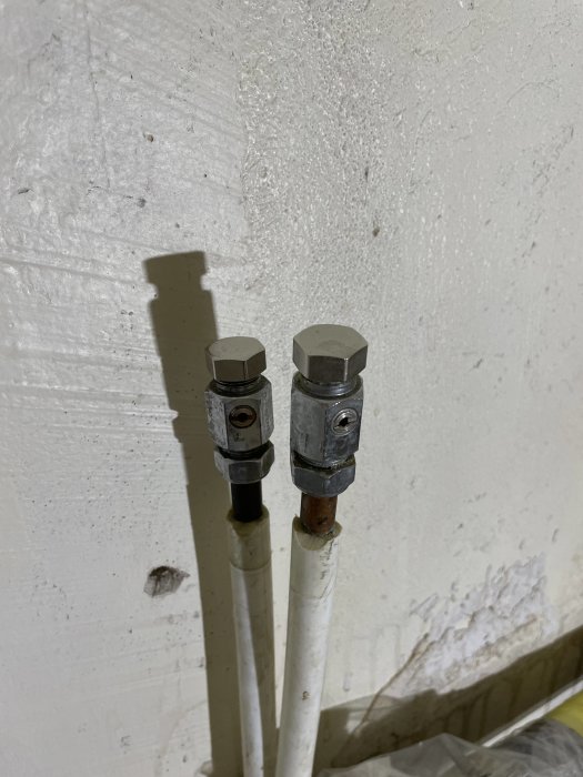 Två kablar fästa på vit vägg med metallkopplingar och skuggor, möjligtvis för telekommunikation eller data.