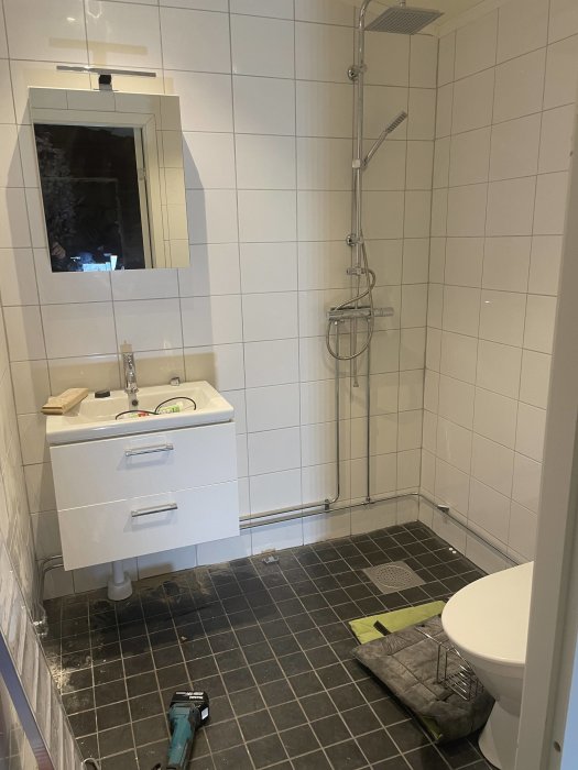 Ett modernt badrum under renovering eller reparation med verktyg och damm på golvet.