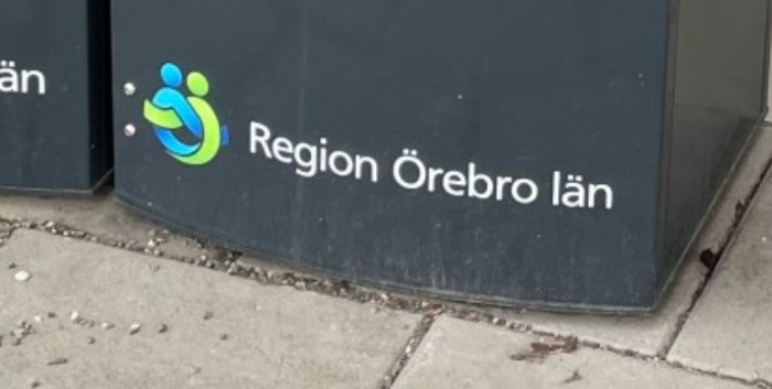 Skylt med text "Region Örebro län" och en logotyp på en trottoar.