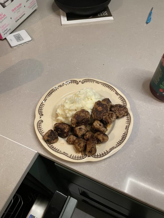 Ett fat med köttbullar och potatismos på ett köksbänk, omgiven av köksartiklar.