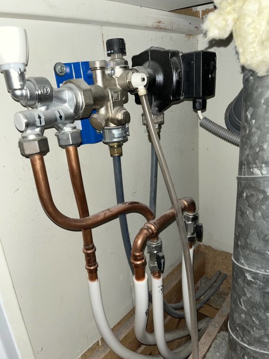 Installation med kopparledningar, ventiler och en svart pump, placerade inne i ett utrymme.