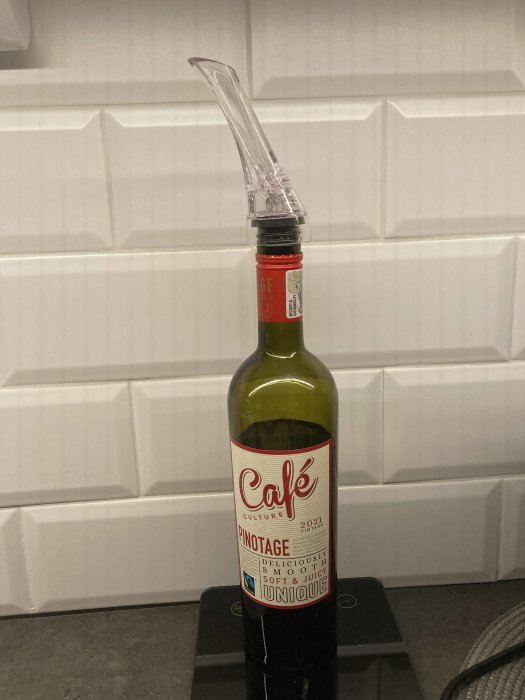Vinflaska med öppningshjälpmedel placerad på köksbänk. Vitt kakel i bakgrunden.