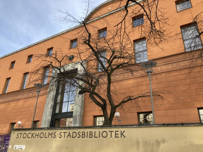 Stockholms stadsbibliotek, orange byggnad, blå himmel, naket träd, utomhus, arkitektur, dagtid.