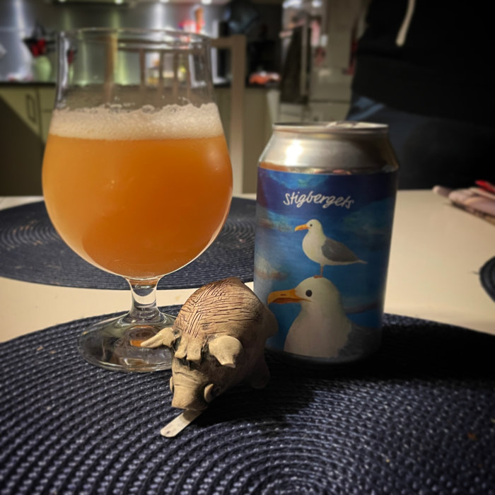 Öl i glas, ölburk med fågelmotiv, trälelefant, mörk yta, suddig bakgrund med person.