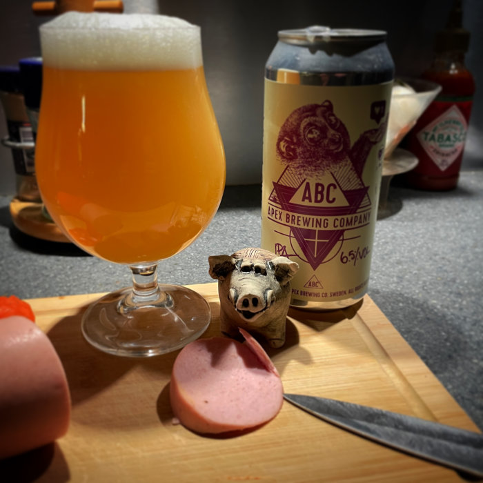 Ölglas, burk från Apex Brewing, skärbräda, falukorv, grisfigur, Tabasco, belysning bakgrund.