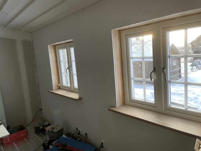 Ett pågående inomhus renoveringsprojekt med fönster och snöig utsikt.