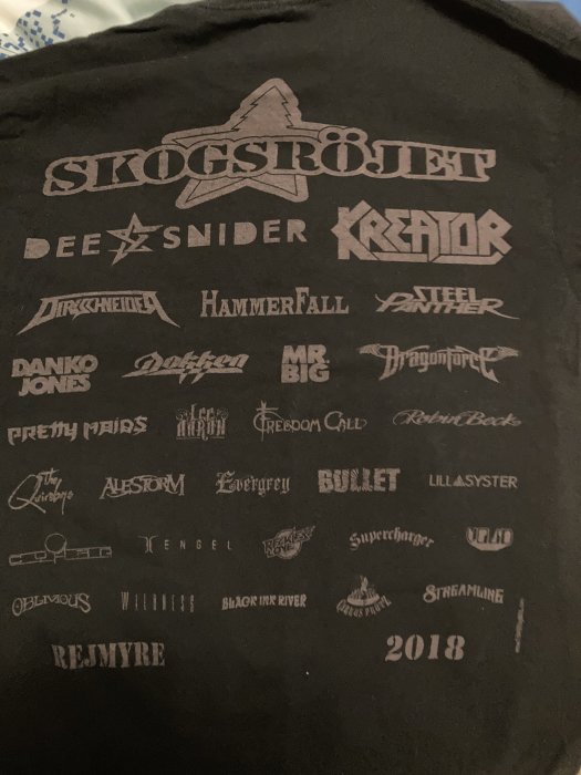 Svart T-shirt med bandnamn och logoer; troligtvis från musikfestival eller konsert, daterad 2018.