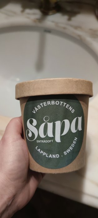 Hållen behållare med texten "Västerbottens Såpa", enträdoft, Lappland Sweden, hålls av en hand.