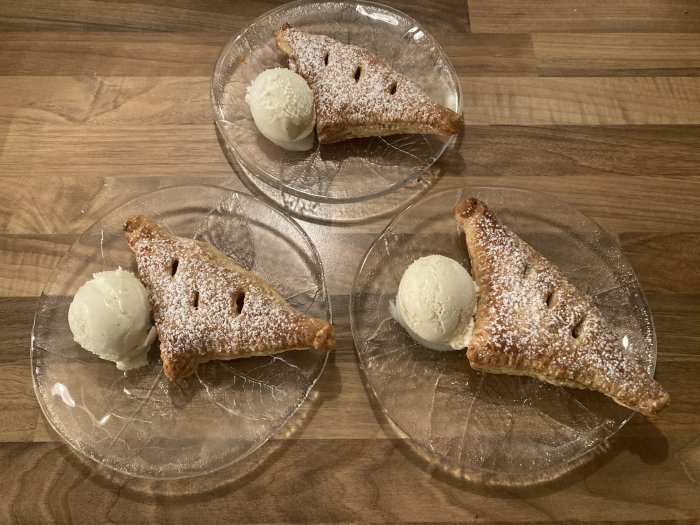 Tre portioner av bakverk och glass på genomskinliga tallrikar mot en träbakgrund.