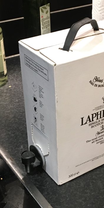 Bag-in-box whisky med tappkran, placerad på köksbänk, bredvid olivolja, enkel och funktionell förpackning.