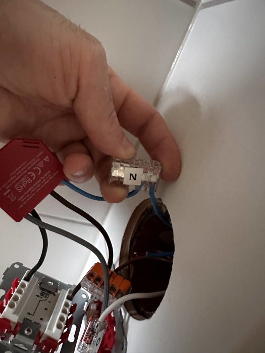 Hand håller nätverkskabel vid vägguttag, elinstallation synlig, RJ45-kontakt, stängningsanordning för strömbrytare.