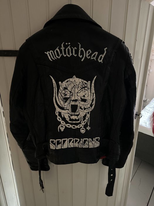 Svart läderjacka med bandloggor "Motörhead" och "Scorpions" på ryggen, upphängd, punkrock stil.