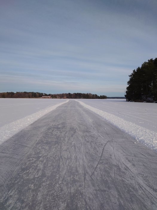 Istäckt sjö med skridskospår, snöklädda skogar och en klar himmel.