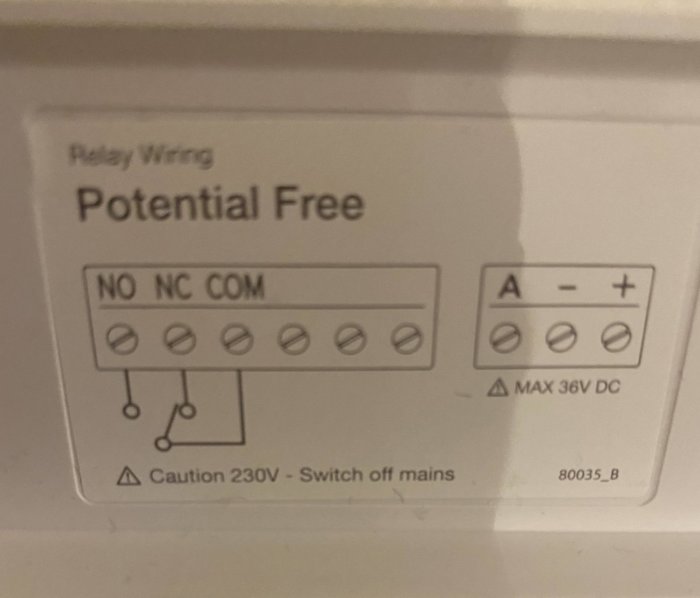 Etikett med elektrisk kopplingsschema för relä, "Potential Free", varningsikoner för högspänning och strömbegränsning.