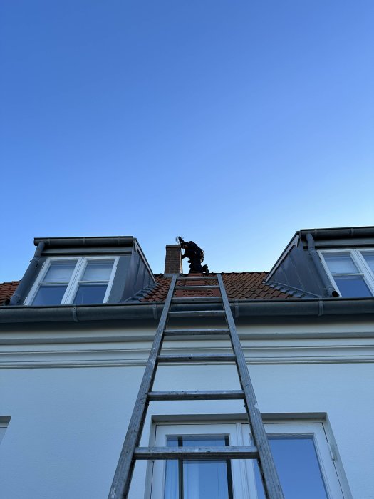 Person på hustak, arbetar, klar himmel, stegar, takfönster, dagtid.