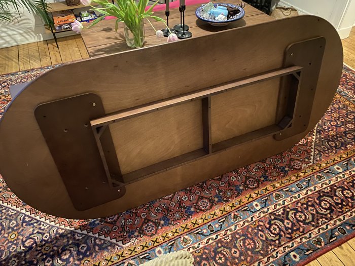 Ett brunfärgat träbord liggande upp och ned på ett orientaliskt mönstrat mattgolv.