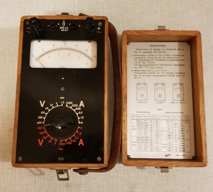 Gammal analog multimeter i träfodral med instruktioner och skalaindelningar, troligen för elektriska mätningar.