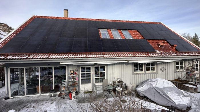 Hus med solpaneler på taket, inglasad uteplats, täckt båt, snörester och trädgårdsdekorationer.