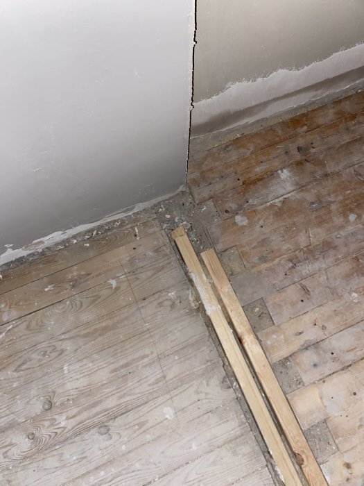 Renoveringsarbete, gammalt trägolv, vägg med spricka, bristfälligt byggnadsarbete eller skada, behov av reparation.