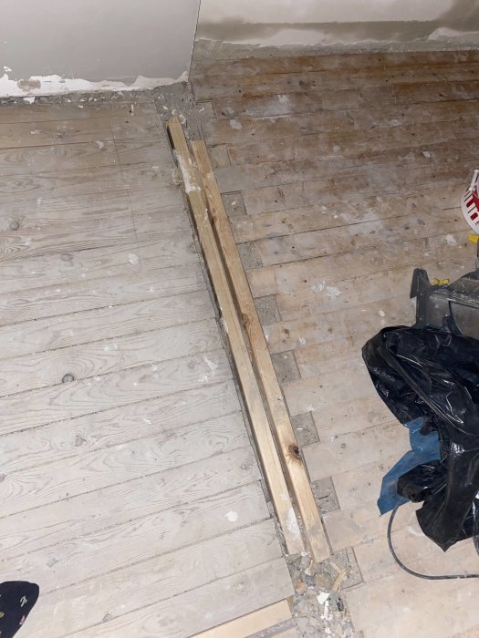 Renoveringsarbete, trägolv delvis avlägsnat, exponerade reglar, byggavfall, verktyg till vänster, renoveringsprojekt pågår.