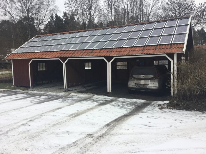 Carport med solpaneler på taket, bil parkerad, snö på marken, vinterdag.