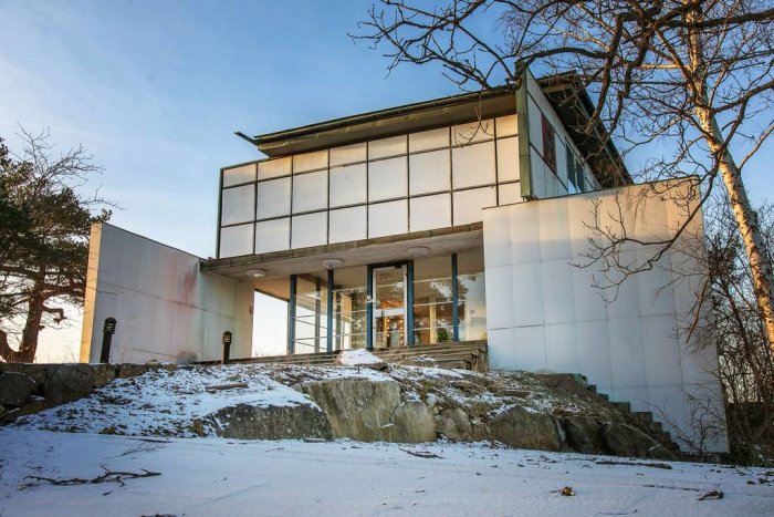 Modern villa på klippa, vinter, träd, snö, arkitektonisk design, stora fönster, klar himmel.