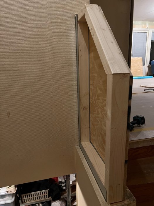 Inomhusbyggarbetsplats med träkonstruktion, plywood, verktyg i bakgrunden, pågående renovering eller bygge.