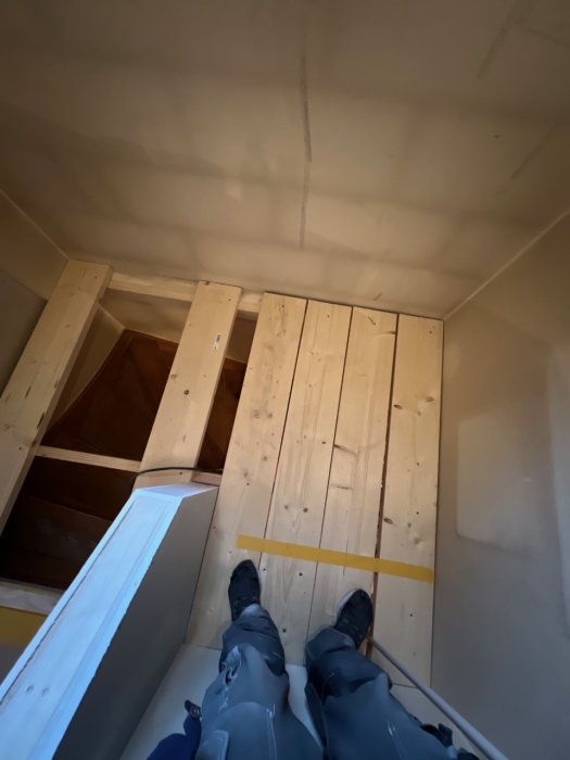Person sedd uppifrån på ny trapp, trästeg, vita räcken, byggarbetskläder, början till övervåning eller vind.