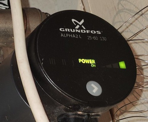 Grundfos Alpha2 cirkulationspump för värmesystem, påslagen med grön indikator, kablar, en del av fläkthjul synlig.