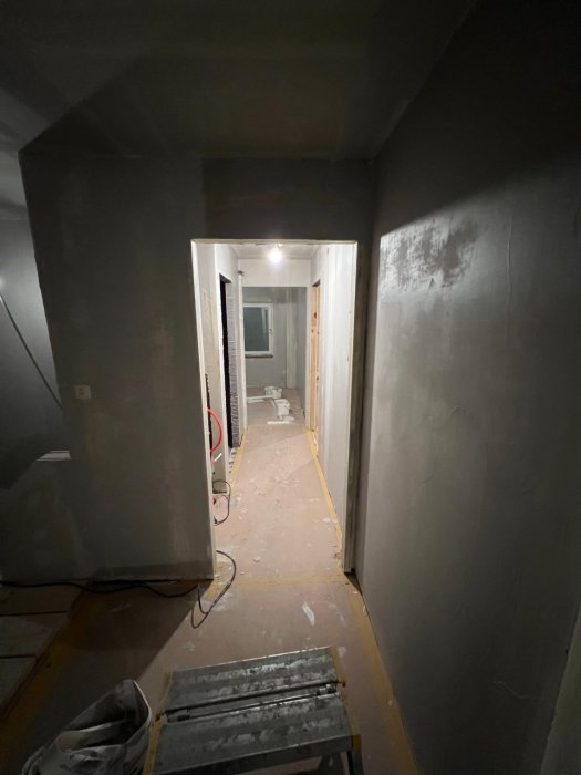 En mörk, smal korridor under renovering med byggmaterial och en stege på golvet.