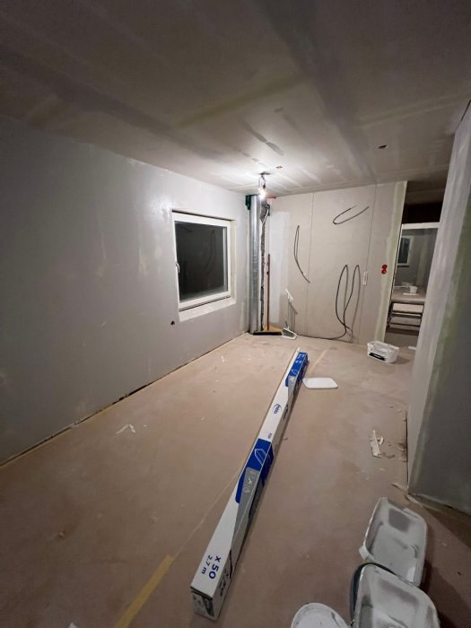 Ett under renovering rum med oslipade gipsväggar, isolering synlig, ogjort golv och byggmaterial.