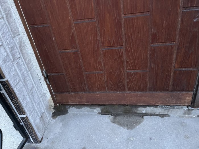 En träfärgad dörr med slitage vid tröskeln, mot en isfläckad betongyta.