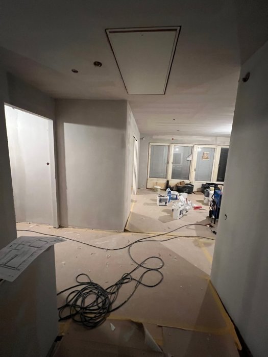 Ett oavslutat korridorsutrymme med byggmaterial, kablar och skyddspapp under renovering eller konstruktion.
