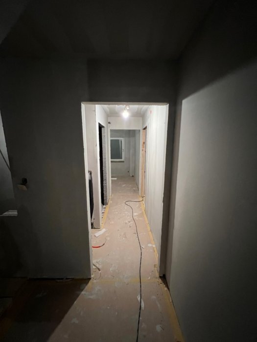 Ett korridor under renovering, nakna golv, väggar målade, öppna dörrar, rör skaft och sladdar synliga.