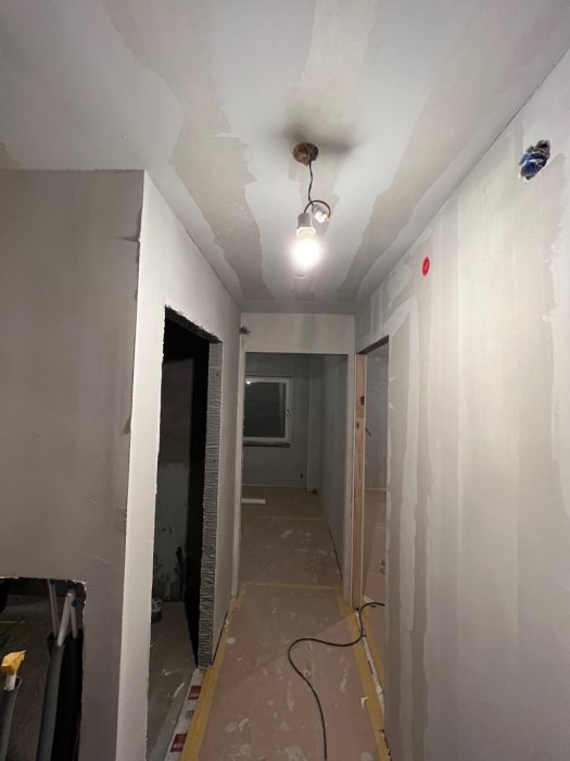 En korridor under renovering med oavslutade väggar, utsatt elektricitet och byggmaterial på golvet.