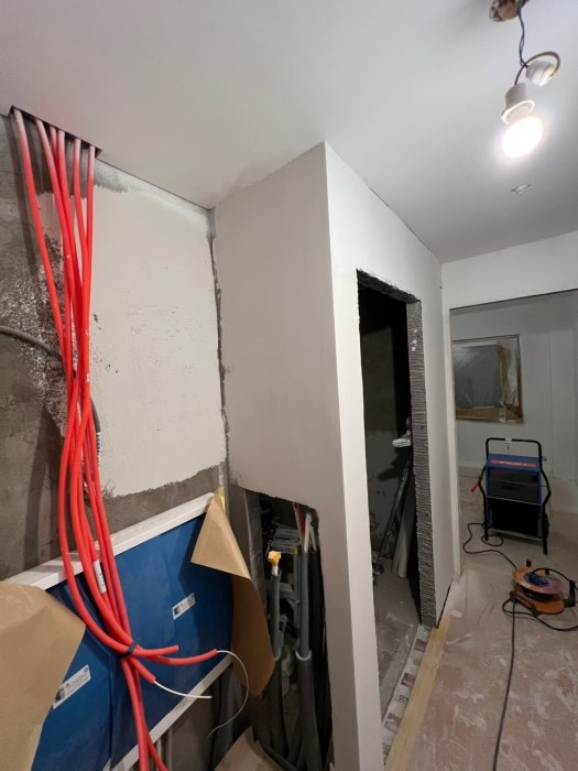Renoveringsarbete pågår inomhus; kablar, oputsade väggar och byggmaterial synliga, arbetsbelysning i bakgrunden.