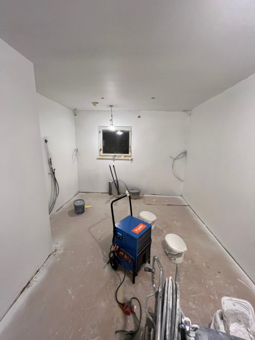 Renoveringsprojekt pågår i rum med maskiner, kablar, byggmaterial och osatt fönster.