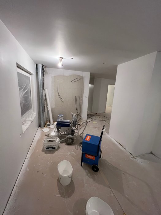 Renoveringsarbete inomhus, ommålningsförberedelser, byggutrustning och skyddsplast på golvet.