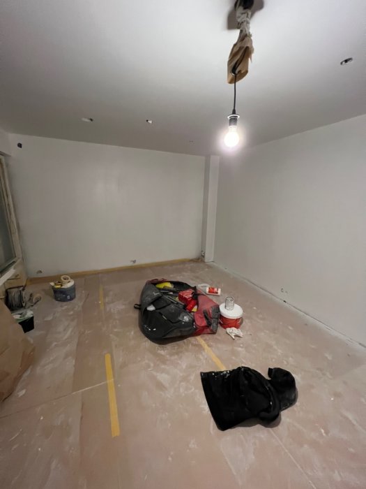 Renoveringsarbete pågår, skyddad golv, väggar målade, eluttag, verktyg och material utspridda, enkel hängande lampa.