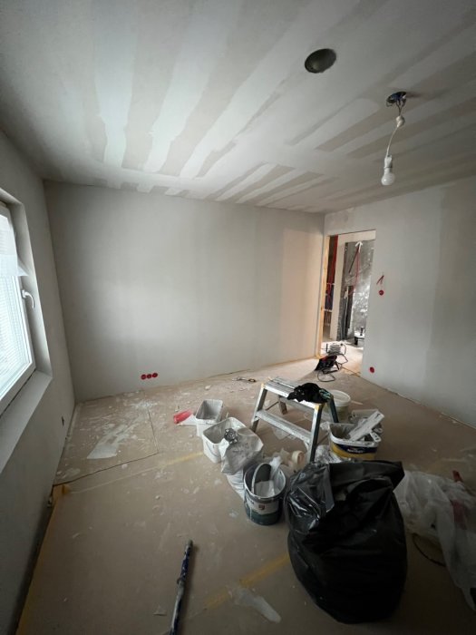 Renoveringsarbete pågår, spackel på väggar, skräp och byggmaterial på golv, oavslutad interiör.