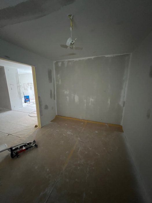 Tomt rum under renovering, väggspackel, osatt golv, takfläkt, nedfallna byggmaterial.