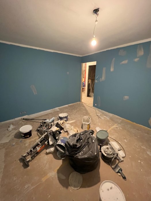 Ett rum under renovering med måleriutrustning och spackel på väggarna.