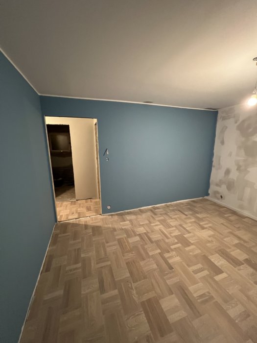 Tomt rum med blå väggar, trägolv, öppen dörr, renovering pågår, oslipad vägg till höger.