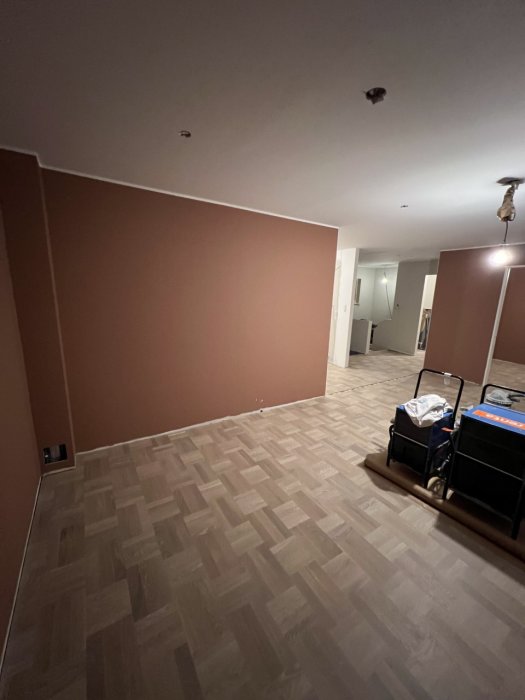 Ett tomt rum med bruna väggar, mönstrat golv och en vagn med lådor.