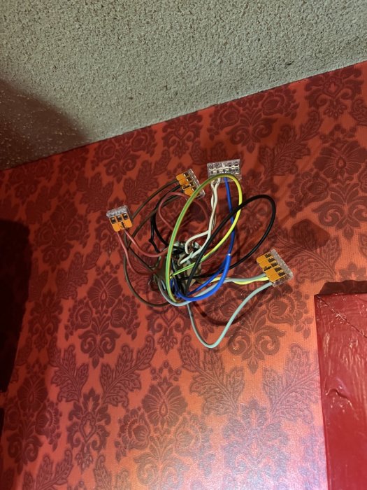 Oorganiserade elledningar och Ethernet-kontakter mot röd vägg med mönster. Oavslutad elektrisk installation.