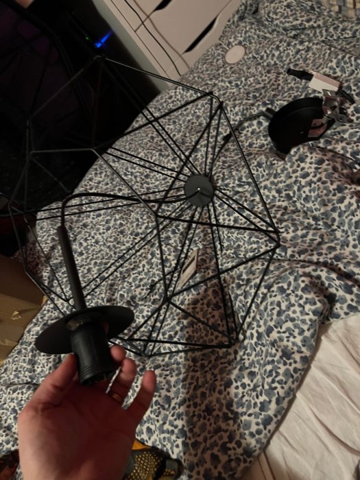En hand håller två fragment av en svart trasig paraply mot en leopardmönstrad säng. Oreda i bakgrunden.