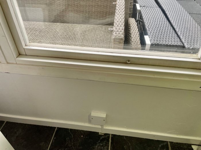 Inomhusvy av ett fönster, fönsterbräda, vit vägg och en glimt av utemöbler genom fönstret.